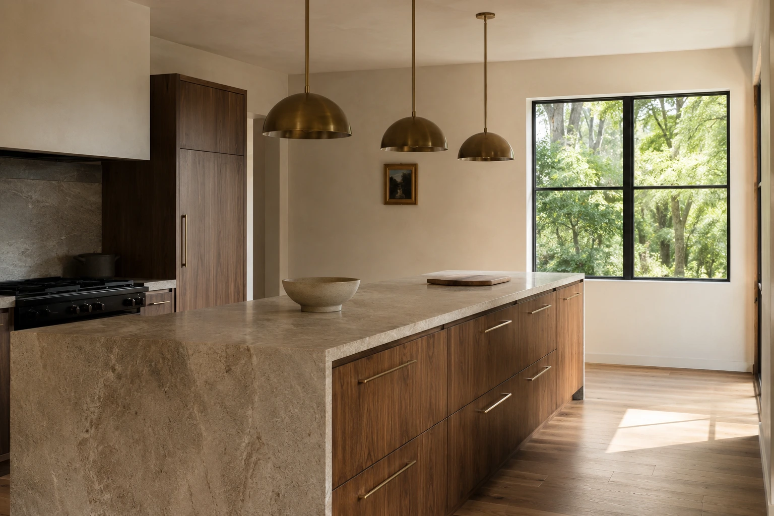 Concept image of a wide warm contemporary kitchen with walnut cabinetry, a honed limestone island and three brushed brass pendant lights, lit by a large window.